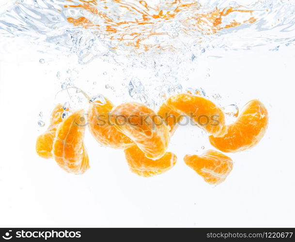 Isolated falling orange segments into water. Peeled pieces of orange fruit in the water isolated on white background. Health concept. Isolated falling orange segments into water. Peeled pieces of orange fruit in the water isolated on white background