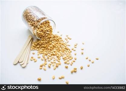Isolated on a white background is a glass jar with golden wax and wooden sticks for depilation.