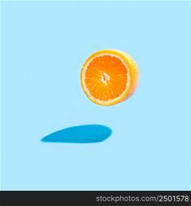 Isolated orange half with a real shadow on blue background. Flying orange on blue.