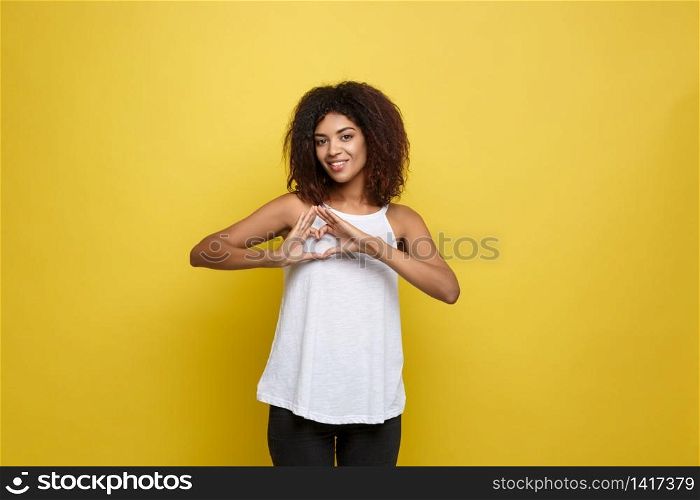 Isolated portrait of beautiful African American make heart symbol by hands. Yellow studio background. Copy Space. Isolated portrait of beautiful African American make heart symbol by hands. Yellow studio background. Copy Space.