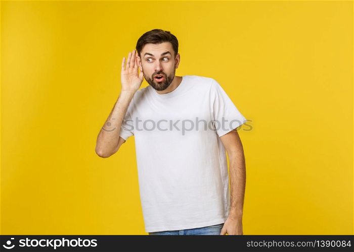 Isolated portrait of smiling young man in casual clothes listening attentively with his palm near ear. Concept of curiosity and eavesdropping.. Isolated portrait of smiling young man in casual clothes listening attentively with his palm near ear. Concept of curiosity and eavesdropping