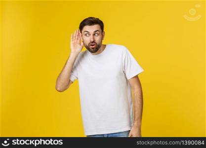 Isolated portrait of smiling young man in casual clothes listening attentively with his palm near ear. Concept of curiosity and eavesdropping.. Isolated portrait of smiling young man in casual clothes listening attentively with his palm near ear. Concept of curiosity and eavesdropping