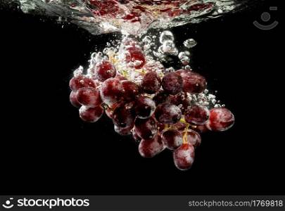 Isolated Red grapes splashing and sinking in water on black background. Isolated Red grapes splashing and sinking in water on black