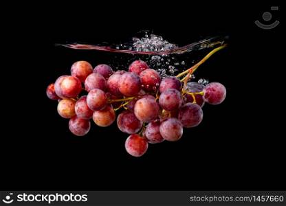Isolated Red grapes splashing and sinking in water on black background with air bubbles.. Isolated Red grapes splashing and sinking in water on black background