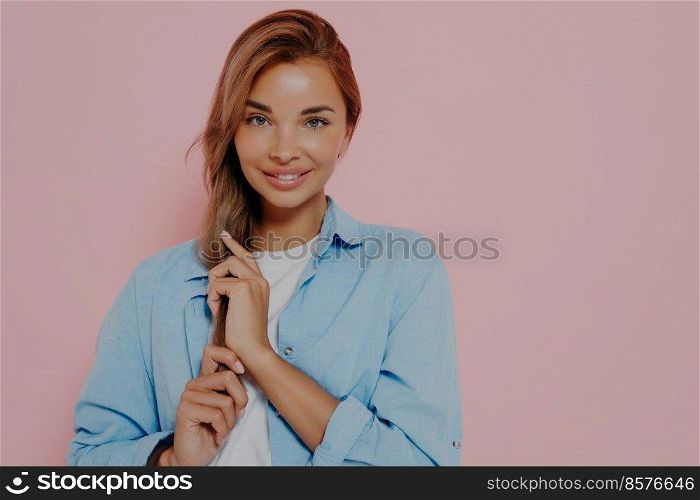 Isolated shot of attractive european student female with long straight hair looking and smiling at camera while touching her hair with hands. Positive human facial expressions and emotions. Isolated shot of attractive european student female with long straight hair