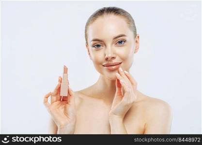 Isolated shot of beautiful girl applies lipstick on lips, has perfect makeup, poses with beauty product, touches face gently, poses shirtless, gets ready for work, poses against white background