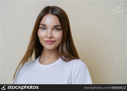 Isolated shot of pleasant looking woman with dark straight hair, wears white t shirt, isolated over brown background, copy space for your advertising content, listens interesting stories and good news