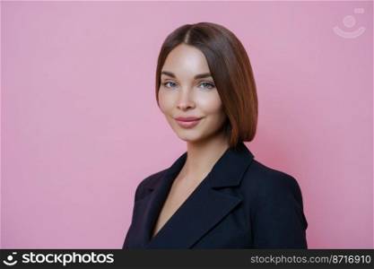 Isolated shot of pretty dark haired woman with healthy glowing skin, dressed formally, going to have formal meeting, wears makeup, poses against pink background. Successful businessewoman indoor