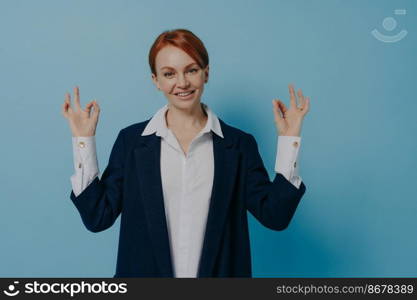 Isolated shot of young cheerful positive red haired business woman in classic outfit showing okay hand gesture, signal of understanding, approval or well-being, raising both hands in ok sign. Isolated shot of young cheerful positive red haired business woman in classic outfit showing okay hand gesture