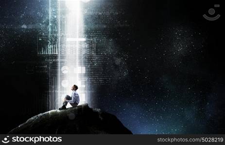 Isolated to find inspiration. Young businessman sitting alone in light on rock top