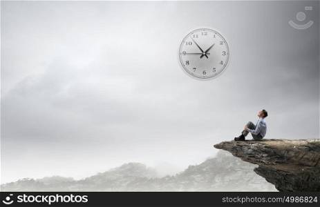 Isolated to find inspiration. Young businessman sitting alone on rock top