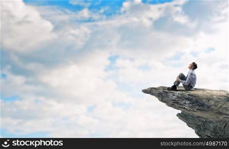 Isolated to find inspiration. Young businessman sitting alone on rock top