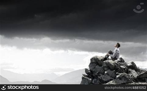 Isolated to find inspiration. Young smiling businessman sitting alone on rock top
