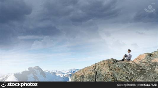 Isolated to find inspiration. Young thoughtful businessman sitting alone on rock top
