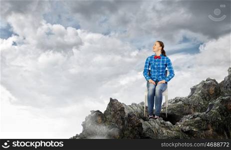 Isolation concept. Young woman in casual sitting on top of rock