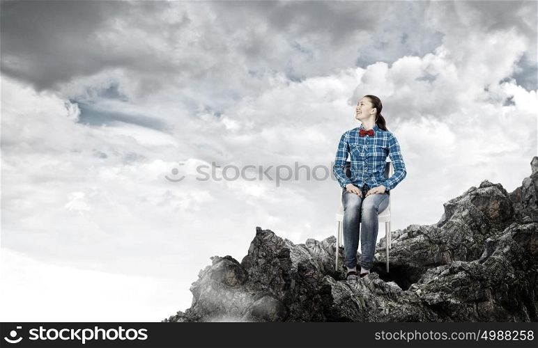 Isolation concept. Young woman in casual sitting on top of rock