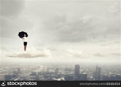 It is crisis time. Young businesswoman with black umbrella standing on cloud