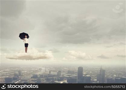 It is crisis time. Young businesswoman with black umbrella standing on cloud