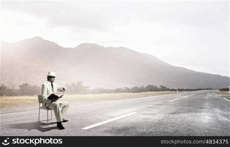 It is high time for business. Young businessman sitting in chair with book in hands