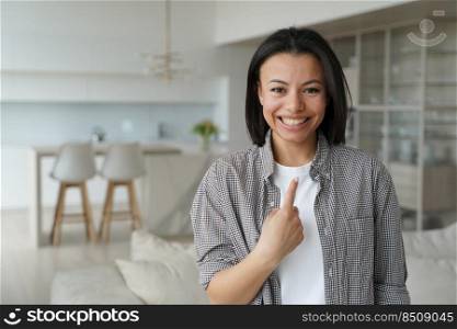 It is me. Happy girl points to herself with finger. Conceptual portrait of young emotional woman. Advertising banner mockup. Smiling european girl in living room at home. Modern interior of apartment.. It is me. Happy young emotional girl points to herself with finger. Advertising banner mockup.