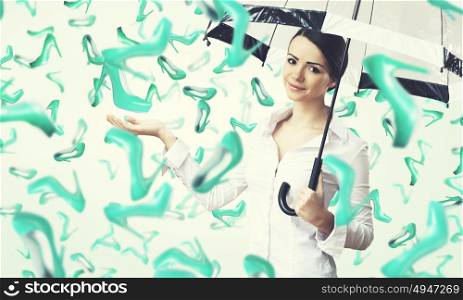 It is rainning shoes. Beautiful young woman with umbrella and falling shoes