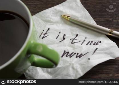 It is time now. Message written on napkin and coffee cup on wooden napkin