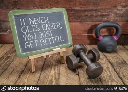 it never gets easier, you just get better - inspirational slogan on a slate blackboard with kettlebell and dumbbells, fitness and lifestyle concept