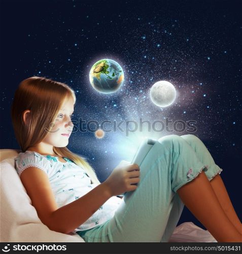 It&rsquo;s bedtime. Girl sitting in bed and playing with tablet pc. Elements of this image are furnished by NASA