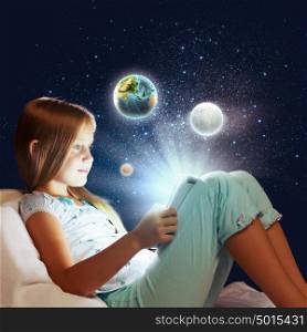 It&rsquo;s bedtime. Girl sitting in bed and playing with tablet pc. Elements of this image are furnished by NASA