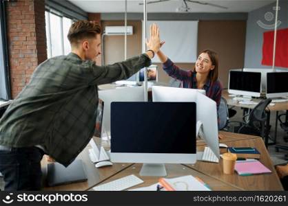 IT specialists high-five each other in office. Web programmer or designer at workplace, creative occupation. Modern information technology, corporate team. IT specialists high-five each other in office