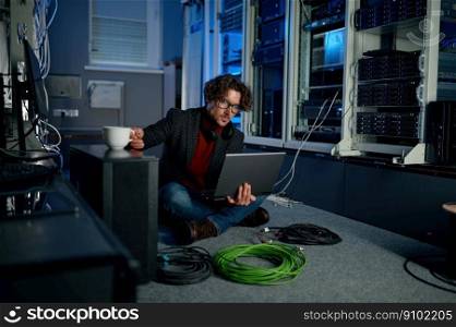 IT technician using laptop while working with essential equipment in data center. IT professional taking coffee break. IT technician using laptop while working in data center
