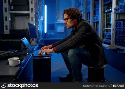 IT technician using laptop while working with essential equipment in data center. IT professional taking coffee break. IT technician using laptop while working in data center