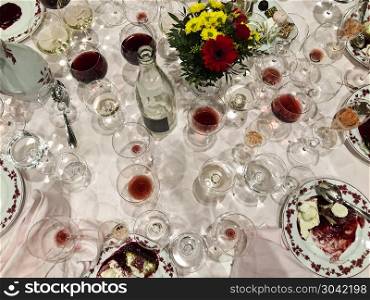 It Was An Elegant Party. After a long and elegant dinner, a table with white tablecloth is full of empty and half-empty wine glasses and half-eaten desserts.