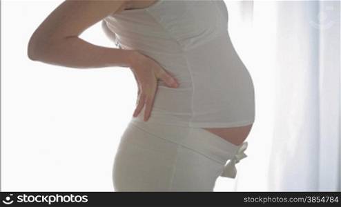 italian 7 months pregnant woman massaging her back. Side view