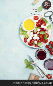 Italian antipasti snack for wine. Mozzarella cheese, fresh basil leaves, tomatoes, olive oil and glasses of red wine on concrete background, top view. Caprese salat