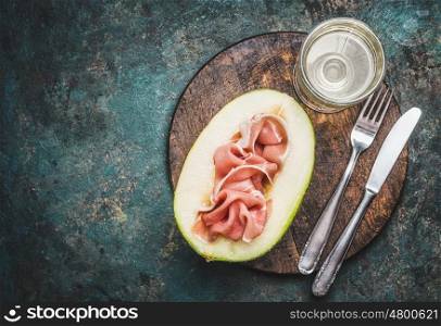 Italian antipasti with ham , melon and wine served with cutlery on rustic background, top view