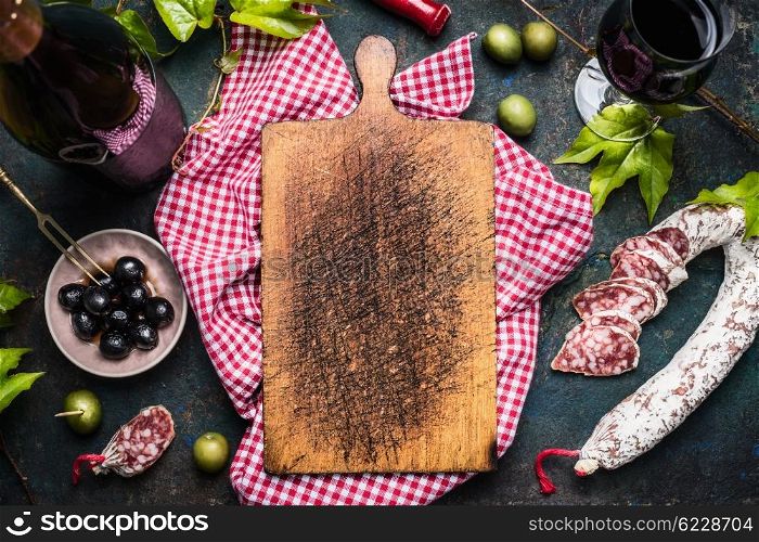 Italian antipasti with olives, red wine and salami around blank old cutting board, top view, place for text. Italian food background