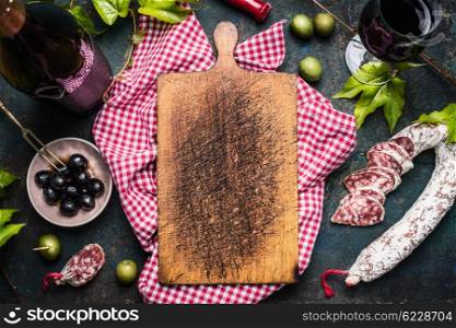 Italian antipasti with olives, red wine and salami around blank old cutting board, top view, place for text. Italian food background