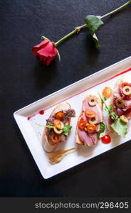 Italian appetizer Carpaccio bread Foie gras and olives, tomato, Pamaham, smoked duck and cranberries sauce in white plate on black table