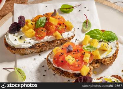 Italian bruschettas with roasted tomatoes, cream cheese, pineapple slices and herbs on a kitchen countertop. Prepared to serve