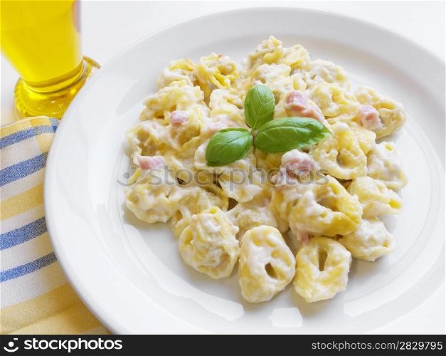 Italian cuisine background. Delicious stuffed pasta tortellini with cream, ham and basil on white dish.