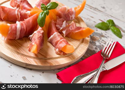 Italian cutting board with prosciutto and melon over a wooden background. Italian cutting board with prosciutto and melon
