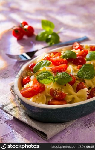 Italian Farfalle pasta with tomatoes and basil over a colored background. Italian Farfalle pasta with tomatoes and basil