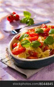 Italian Farfalle pasta with tomatoes and basil over a colored background. Italian Farfalle pasta with tomatoes and basil