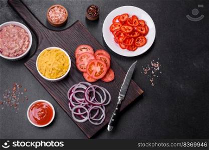 Italian food background. Ingredients on dark background. Cooking background. Raw ingredients for delicious Italian pasta: tomatoes, minced meat, pasta, spices and herbs