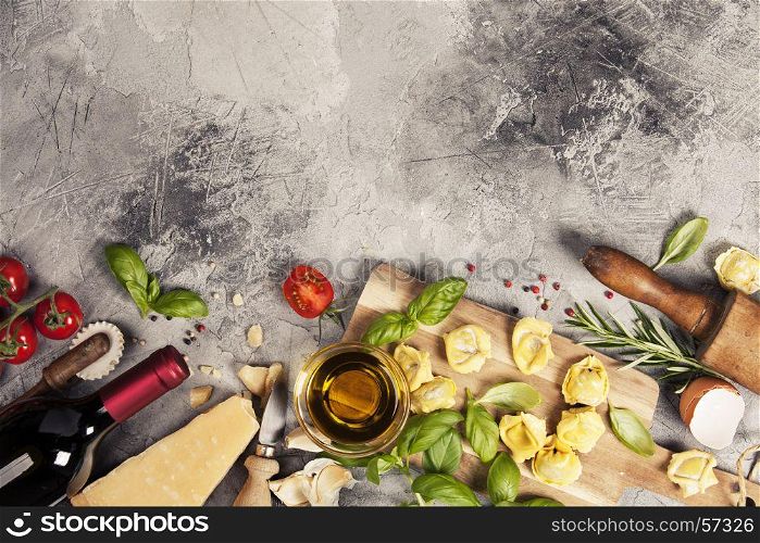 Italian food background with ravioli, vine tomatoes, basil, spaghetti, spinach, onion, parmesan, olive oil, garlic, peppercorns, rosemary and wine. Slate background