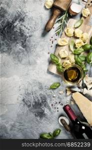 Italian food background with ravioli, vine tomatoes, basil, spaghetti, spinach, onion, parmesan, olive oil, garlic, peppercorns, rosemary and wine. Slate background