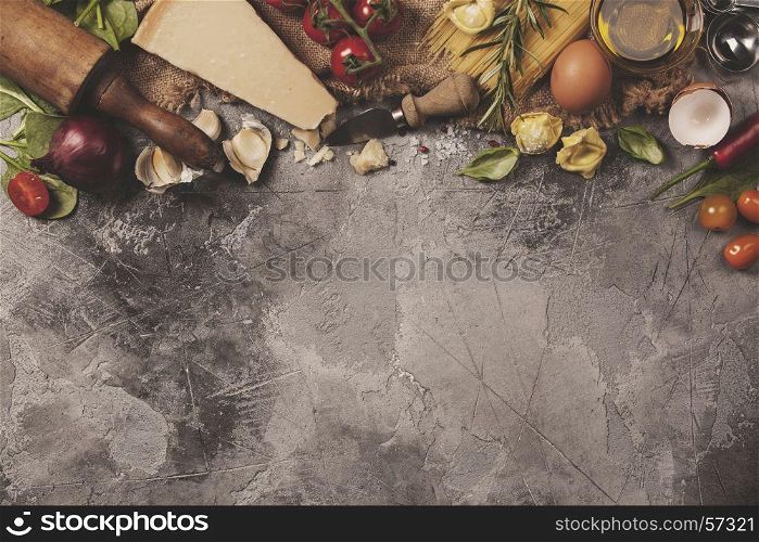 Italian food background with vine tomatoes, basil, spaghetti, spinach, onion, parmesan, olive oil, garlic, peppercorns, rosemary and eggs. Slate background