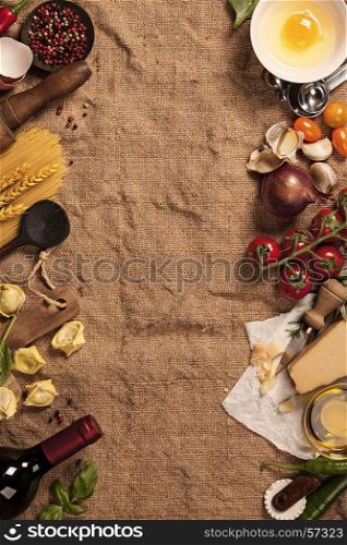 Italian food background with vine tomatoes, basil, spaghetti, spinach, onion, parmesan, olive oil, garlic, peppercorns, rosemary and eggs. Burlap background