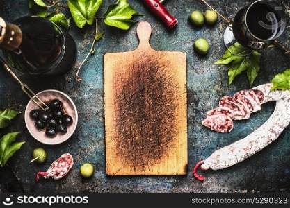 Italian food background with wine, olives and sausage around wooden cutting board, top view